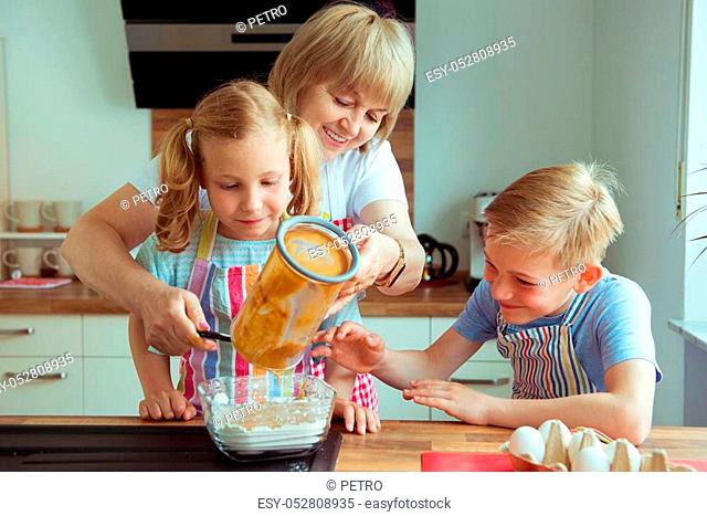Happy grandmother with her grandchildren having fun during baking muffins and cookies