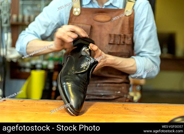 Male cobbler holding shoe while polishing at workshop