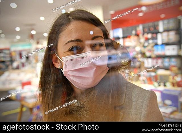 Topic picture part of lockdown in the coronavirus pandemic on November 26th, 2020. A young woman with face mask, mask is in a shop behind a pane of glass