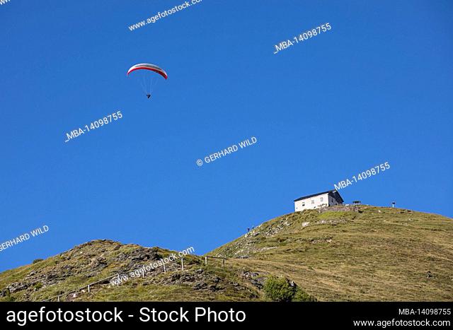 paraglider over the summit of the helm and the helmhütte (2, 433 m), carnic alps, south tyrol, italy
