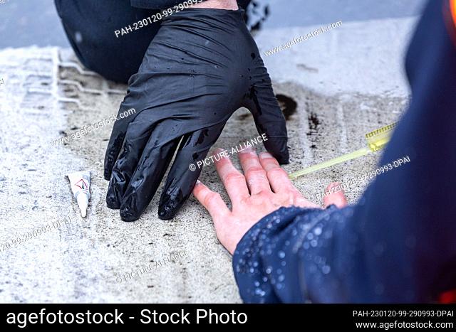 20 January 2023, Saxony, Dresden: A policeman uses olive oil to detach the hand of a ""Last Generation"" activist from the road