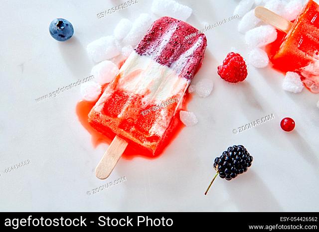 Ice cream popsicles from homemade greek yogurt and fresh organic berries over ice with berries on marble background, top view