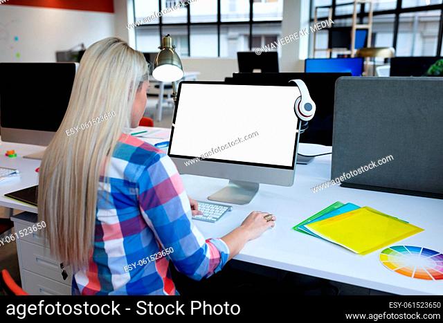 Caucasian businesswoman sitting at desk in creative office using desktop computer