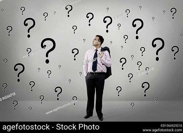 A corporate employee in formal business suit standing confused amidst question marks