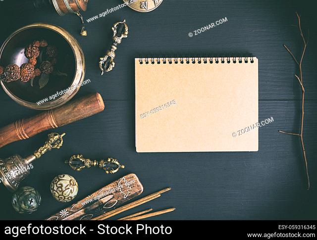 Asian religious musical instruments for meditation and alternative medicine, blank notebook with brown sheets on a black wooden background, top view