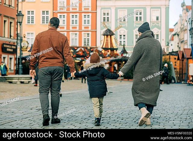 Mother and father holding hands with son and walking on footpath at Christmas market