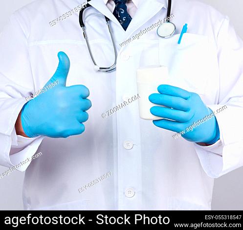 male doctor in a white medical coat and blue latex gloves holds a white plastic jar of pills, close up