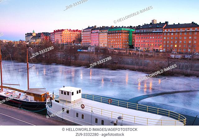 Boats frozen in the ice of Karlberg Lake (Karlbergssjon) at dawn with colourful facades of the Atlas district in the background, Norrmalm, Stockholm, Sweden