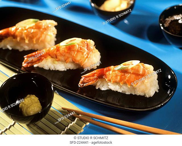 Nigiri with shrimp tails on black platter, chopsticks