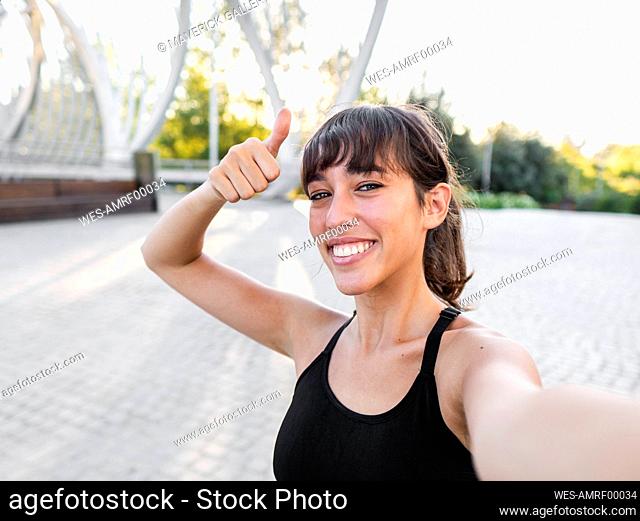 Happy young woman gesturing thumbs up at footpath