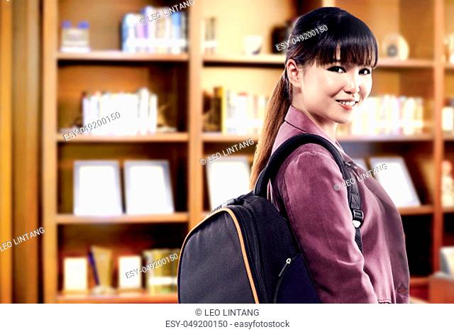 Asian student woman with backpack standing and look back in the university library. Back to School concept