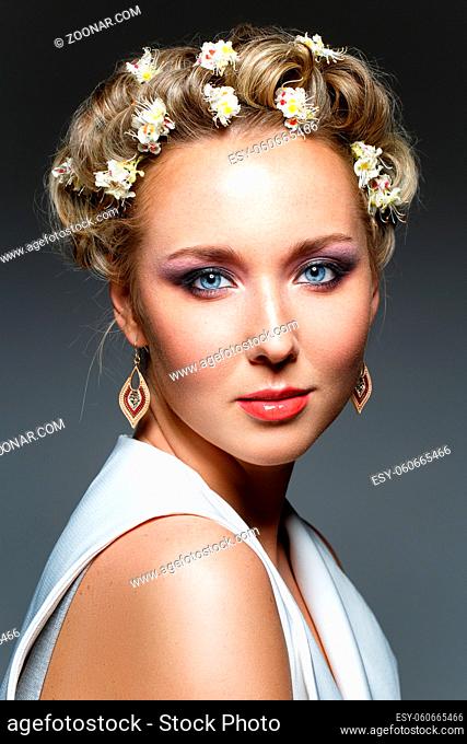 beautiful blond young woman in white top with blooming sweet chestnut flowers in hair. studio beauty shot. copy space