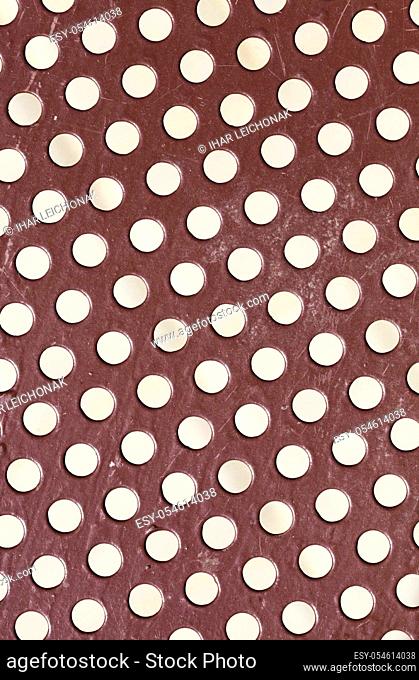painted metal surface with round shaped holes for ventilation or cheapening construction, used in metal construction on the street, close up