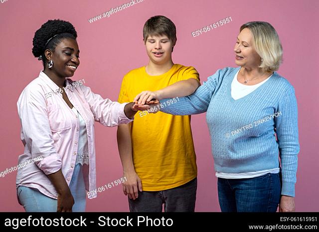 Support. Smiling two women and guy with down syndrome standing with outstretched arms touching with palms on light background