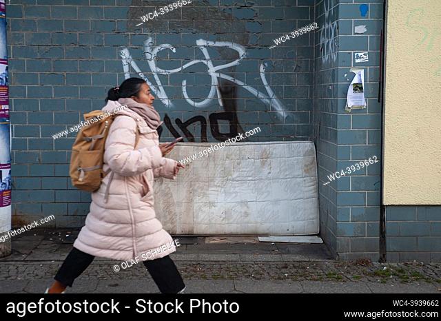 Berlin, Germany, Europe - A woman walks past an old, filthy and illegally discarded mattress that leans against a building wall smeared with graffiti at the...