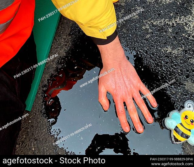 17 March 2023, Cologne: A climate activist has his hand stuck on a road in Cologne. Activists from the climate group Last Generation got their hands stuck on a...