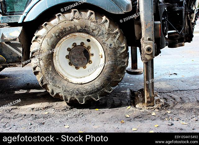 Tractor strong outrigger stabilizing legs extended to stabilize and steady state when digging the soil under the road repair