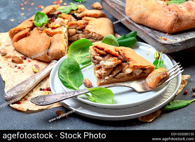 Piece of traditional pie (galette) with chicken, mushrooms, onions served on a plate with fresh spinach and pistachios, selective focus