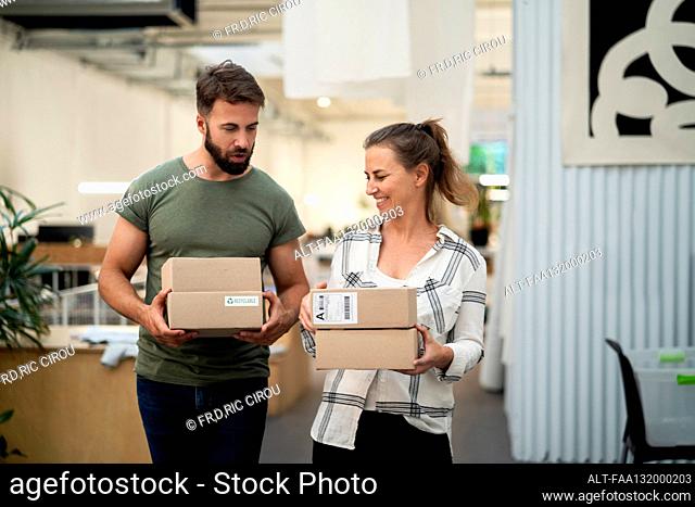 Two coworkers carrying cardboard boxes while walking in office