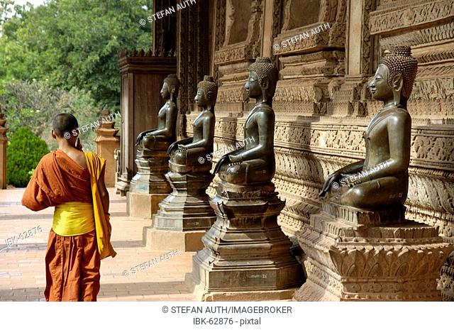 Young monk walks along old Buddha statues temple Haw Pha Kaew Vientiane Laos