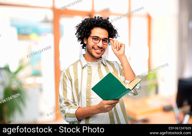 happy young man in glasses reading book at office