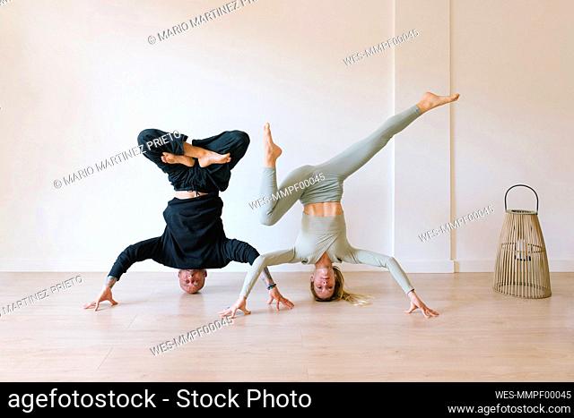 Friends practicing headstand poses in front of wall at yoga studio