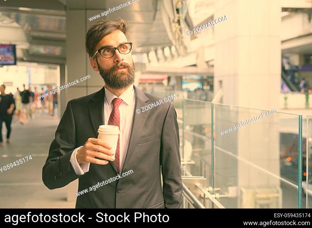 Portrait of young handsome bearded Persian businessman relaxing around the city of Bangkok