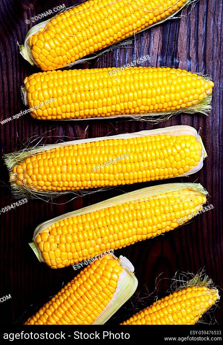 Fresh corn cobs on a brown wooden background, view from above