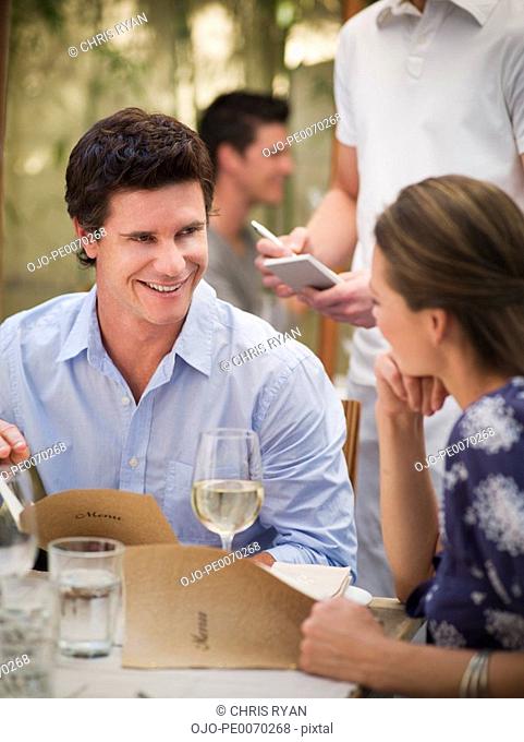 Waiter taking order from couple with menus at restaurant table