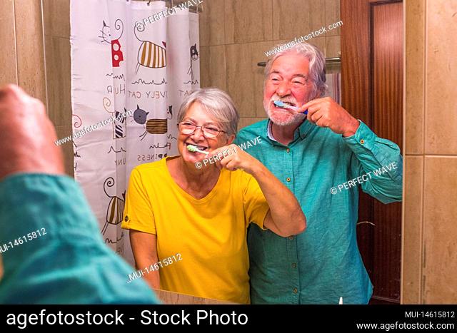 couple of two happy and smiling seniors brushing their teeth of they each other together at home in the bathroom - self care and taking care of theyself