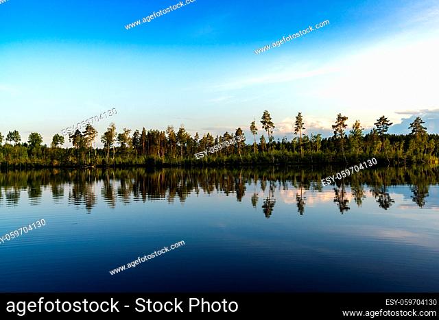 Landscape of calm idyllic deep blue lake with forest on the shore and reflections of trees in the water