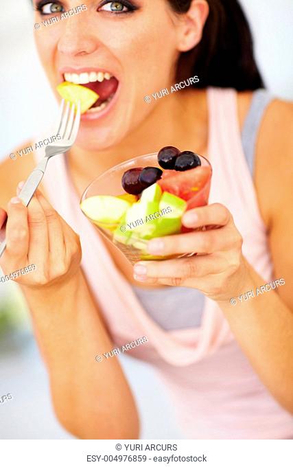 An attractive young woman eating a piece of apple from her fruit salad
