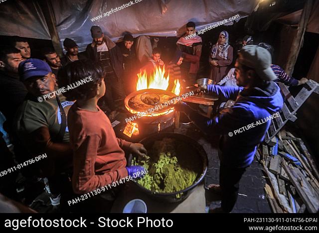 30 November 2023, Palestinian Territories, Khan Yunis: People gather around a Falafel vendor, who fries Falafel over a wood fire due to the lack of cooking gas