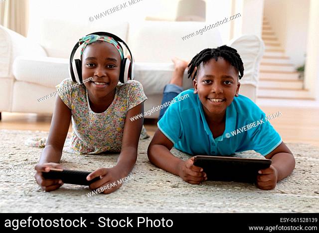 Smiling african american brother and sister wearing headphones lying on floor using smartphones