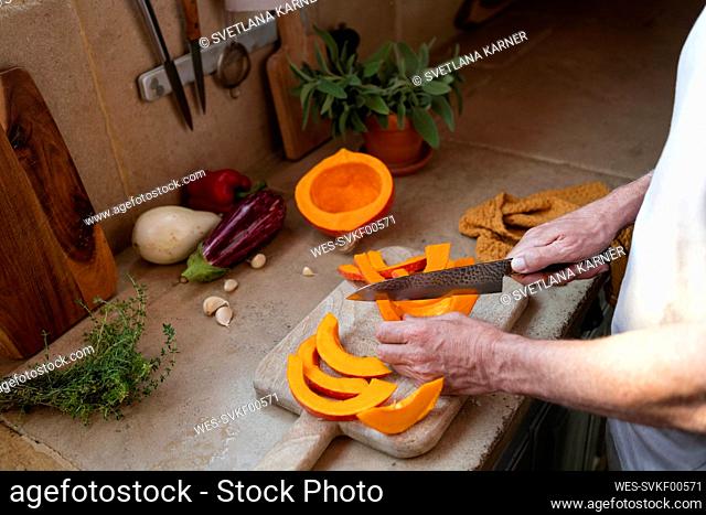 Hands of man cutting pumpkin on board in kitchen