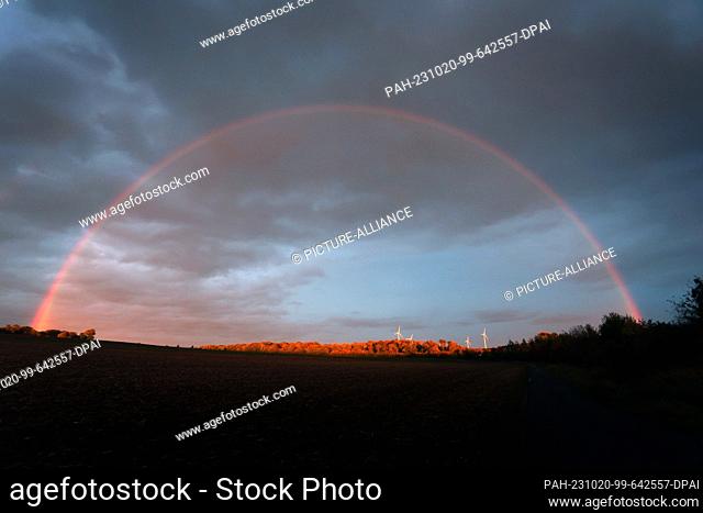 20 October 2023, Bavaria, Biebelried: A rainbow stretches in the evening sun over four wind turbines standing in an autumn landscape