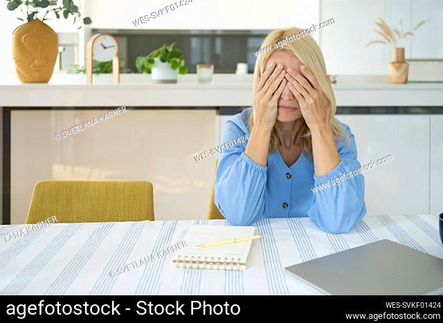 Tired freelancer with head in hands sitting at table in home office