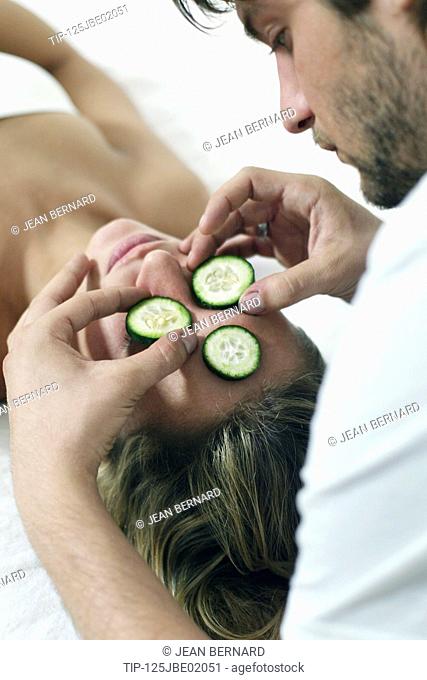 Man applying slice of cucumber on her girfriend's face