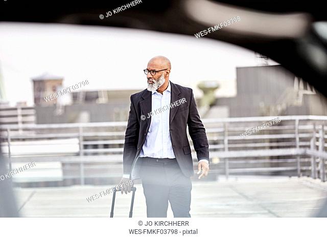 Businessman with trolley bag walking to his car