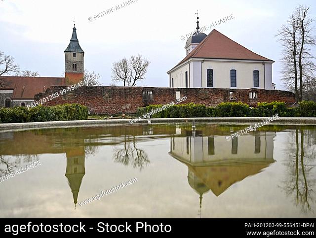 01 December 2020, Brandenburg, Altlandsberg: The town church (l) and the castle church are reflected in the water of a fountain on the grounds of the former...