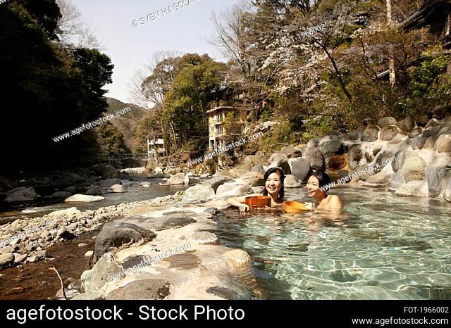 Happy young women soaking in sunny Onsen pool, Izu, Japan
