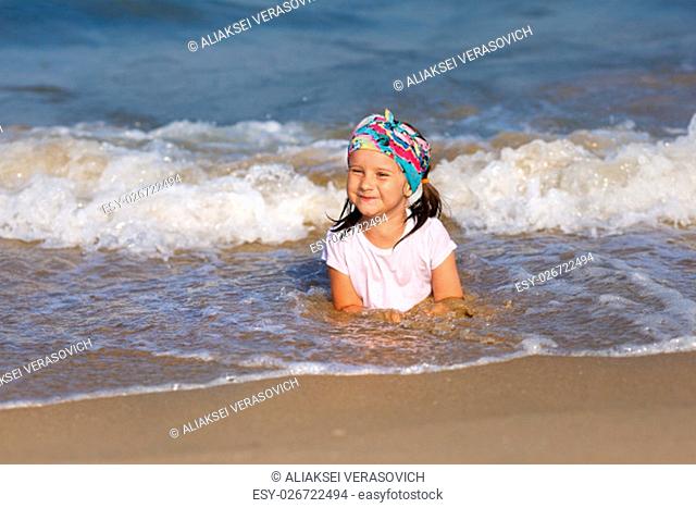 Smiling child in a white t-shirt lying in water on the beach. Shallow depth of field. Focus on the model's face