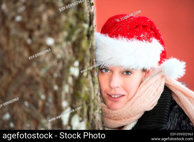 Junge Frau mit Weihnachtsmütze und warmen Schal in der Weihnachtszeitlächelt den Betrachter an. Young woman with christmas hat an warm scarf