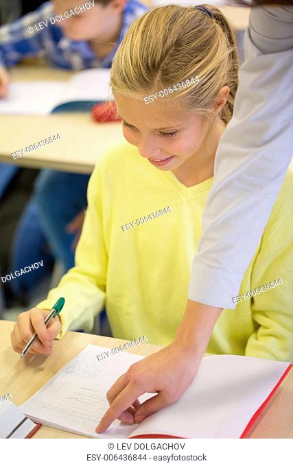 education, elementary school, learning and people concept - teacher helping school girl writing test in classroom