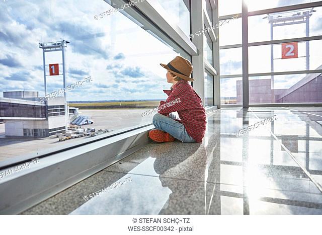 Boy sitting behind windowpane at the airport looking at airfield