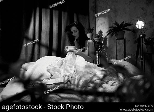beautiful young woman drinking her coffee in her bedroom in the morning. black and white