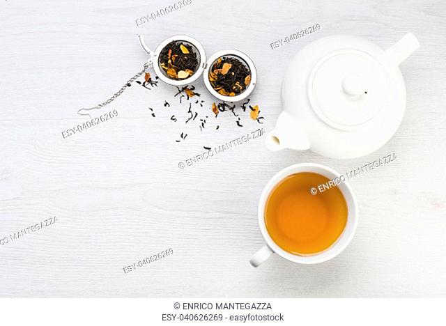 cup of tea with teapot and open infuser with black tea on table