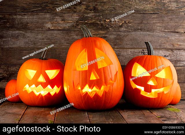 Three Halloween pumpkins head jack o lantern and candles on wooden table background
