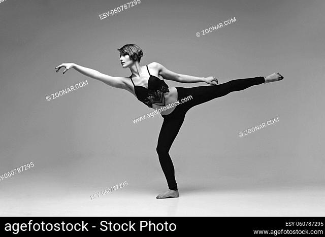 Beautiful young woman dancer making modern dancing elements. studio shot on grey background. copy space. monochrome