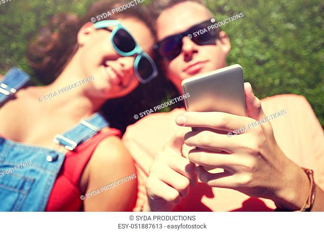 teenage couple with smartphone lying on grass